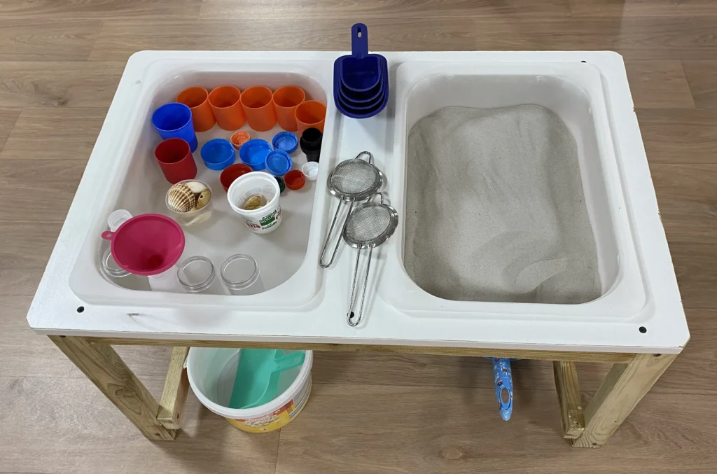 table avec deux compartiment, un avec du sable fin et l'autre avec des outils de transvasement