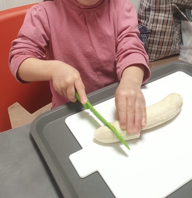activité de vie pratique avec une enfant qui découpe une banane avec du matériel adapté